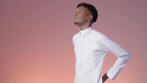 The need for treatment for back and spine pain, feeling of pain and physical aches and pains, fatigue, exhaustion and feeling sick, portrait of a Saudi Arabian Gulf man wearing traditional thobe, putting his hand on his back, colored background