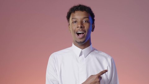 الاندهاش من امر ما، شاب عربي خليجي سعودي مبتسم يرتدي الثوب التقليدي يشير بإصبع السبابه، الوقوف بثقه في النفس، ايماءات الفرح والسرور، خلفيه ملونه