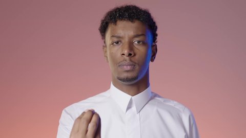 Gestures of slowness and lack of haste, a young Saudi Arabian Gulf man wearing traditional thobe gestures with his hand to not rush, features of masculinity and seriousness, colored background