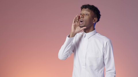 A young Saudi Arabian Gulf man wearing a Saudi thobe puts his hand on the side of his mouth directing his voice to someone, a Saudi man calling out loudly, gestures of confidence and enthusiasm, colorful background