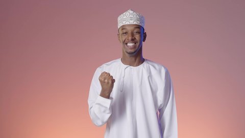 Expressions of joy and happiness, pride and feeling happy, facial expressions indicating excessive enthusiasm, an Arab Gulf Omani man wearing a dishdasha and a sleeve raising his hand up in encouragement