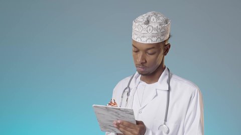 تدوين نتائج الفحوصات بالسجل الطبي، طبيب عربي خليجي عماني يرتدي الدشداشة والكمة والمعطف الأبيض يحمل بيده ملفات المرضى، إعداد التقارير الطبية