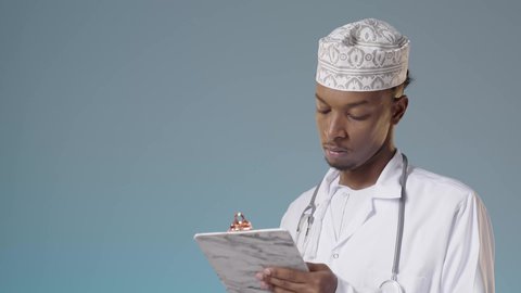 مراجعة ملفات المرضى، تدوين نتائج الفحوصات بالسجل الطبي، طبيب عربي خليجي عماني يرتدي الدشداشة والكمة و المعطف الأبيض و يضع السماعة الطبية و يقوم بتدوين الملاحظات