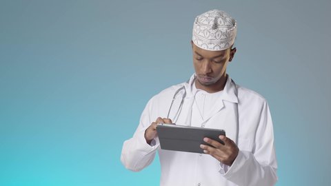 استخدام الاجهزة التقنية الحديثة في مجال الطب، قراءة التقارير الطبية عبر التابلت, طبيب عربي خليجي عماني يرتدي الدشداشة والكمة والمعطف الأبيض و يقوم بمراجعة نتائج الفحوصات بالسجل الطبي