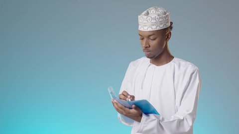 تدوين بعض من الملاحظات, اعداد التقارير الخاصة بالعمل، مجموعة من الاوراق البيضاء، مراجعة ومتابعة الخطط والمشاريع المكتبية بإيماءات التركيز, شاب عربي خليجي عماني يرتدي الدشداشة والكمة يقرأ بتمعن و اهتمام