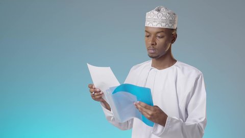 اعداد التقارير الخاصة بالعمل، مجموعة من الاوراق البيضاء، مراجعة ومتابعة الخطط والمشاريع المكتبية بإيماءات التركيز, شاب عربي خليجي عماني يرتدي الدشداشة والكمة يقرأ بتمعن و اهتمام