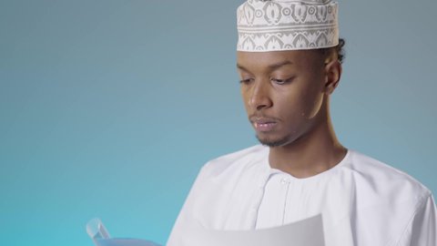 التدقيق في قراءة الملاحظات, مجموعة من الاوراق البيضاء، مراجعة ومتابعة الخطط والمشاريع المكتبية بإيماءات التركيز, شاب عربي خليجي عماني يرتدي الدشداشة والكمة يقرأ بتمعن و اهتمام