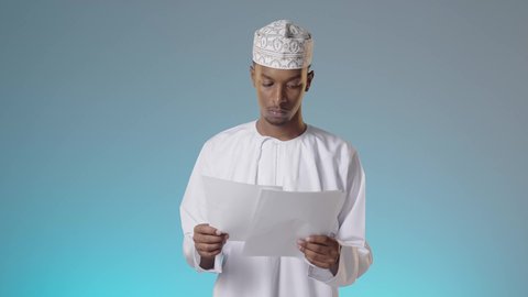 مجموعة من الاوراق البيضاء، مراجعة ومتابعة الخطط والمشاريع المكتبية بإيماءات التركيز, شاب عربي خليجي عماني يرتدي الدشداشة والكمة يقرأ بتمعن و اهتمام