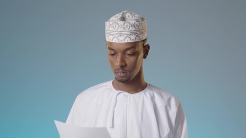 القراءة بتمعن و اهتمام، التزود بالعلم والمعرفة، شاب عربي خليجي عماني يرتدي الدشداشة والكمة  يحمل بيده مجموعة من الاوراق البيضاء، مراجعة ومتابعة الخطط والمشاريع المكتبية بإيماءات التركيز