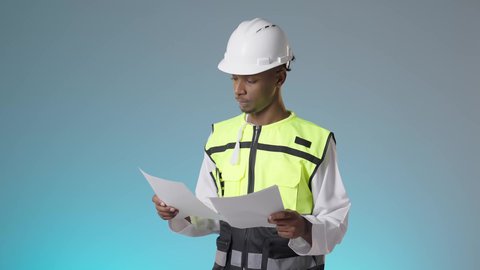 Working in the fields of architectural engineering, professions and jobs for young people in the Sultanate, an Arab Gulf Omani engineer wearing a reflective vest and a white helmet and holding a project plan in his hands