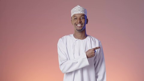 تحديد موقع او هدف معين, الإشارة والتوجيه الى مكان ما، رجل عربي خليجي عماني يرتدي الدشداشة والكمه يقف مبتسما ويشير باصبع السبابه الى مكان ما