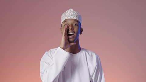 النداء والكلام والتحدث بصوت مرتفع، رجل عربي خليجي عماني مبتسم يرتدي الدشداشة و الكمه يضع يده على فمه بإيماءات المناداة لشخص ما، دردشة ومحادثات وتواصل اجتماعي