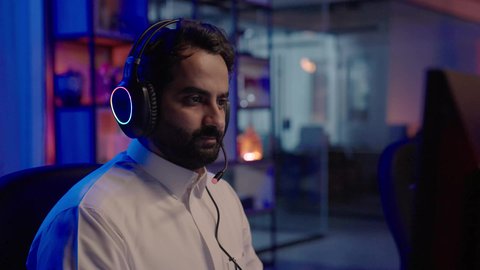 تحرير مقطع فيديو قصير باستخدام تقنيات رقمية حديثة، متابعة الصوت والصورة على شاشة الكمبيوتر، تصوير مقرب من الخلف لمونتير عربي خليجي سعودي يرتدي الثوب الابيض وسماعات الرأس يقوم بالتأمل والإبداع الفني أمام الشاشة