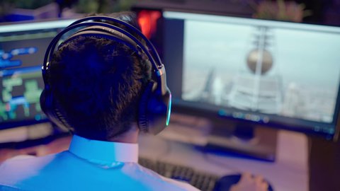 مفهوم الإخراج المرئي، متابعة الصوت والصورة على شاشة الكمبيوتر، استخدام برامج تحرير متطورة لإنتاج الفيديوهات، تصويرمقرب من الخلف  لمونتيرعربي خليجي سعودي يرتدي الثوب الابيض وسماعات الرأس يقوم بالتأمل والإبداع الفني أمام الشاشة