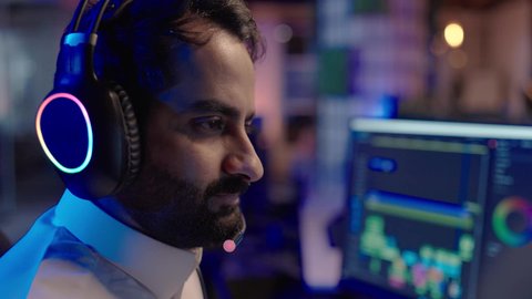 متابعة الصوت والصورة على شاشة الكمبيوتر، تعابير الانسجام مع المؤثرات الصوتية والمرئية، استخدام برامج تحرير متطورة لإنتاج الفيديوهات، تصوير مقرب لمونتير عربي خليجي سعودي يرتدي الثوب الابيض وسماعات الرأس يقوم بالتأمل والإبداع الفني أمام الشاشة