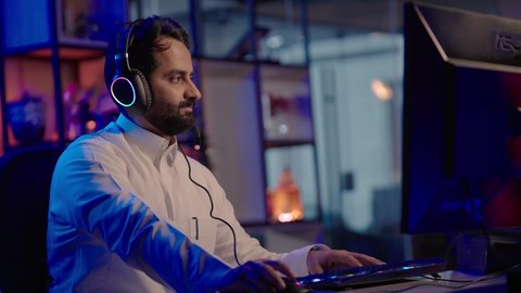 تنظيم المشاهد وإضافة المؤثرات، إيماءات الاندماج و التركيز، استخدام برامج تحرير متطورة لإنتاج الفيديوهات، تصوير لمونتيرعربي خليجي سعودي يرتدي الثوب الابيض وسماعات الرأس يستخدم لوحة المفاتيح والفأرة للتحكم ببرامج المونتاج