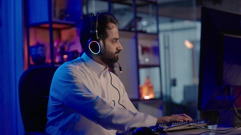 النقر على لوحه المفتايح ،إيماءات الاندماج و التركيز، استخدام برامج تحرير متطورة لإنتاج الفيديوهات، تصوير لمونتيرعربي خليجي سعودي يرتدي الثوب الابيض وسماعات الرأس يقوم بالتأمل والإبداع الفني أمام الشاشة