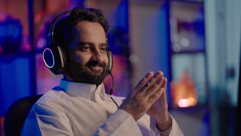 تعابير الانسجام مع المؤثرات الصوتية والمرئية، استخدام برامج تحرير متطورة لإنتاج الفيديوهات، تصويرمقرب لمونتيرعربي خليجي سعودي يرتدي الثوب الابيض وسماعات الرأس يقوم بالتأمل والإبداع الفني أمام الشاشة