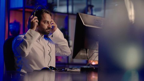 الإبداع في مجال الميديا، استخدام برامج تحرير متطورة لإنتاج الفيديوهات، التأمل والإبداع الفني أمام الشاشة، تصوير لمونتير عربي خليجي سعودي يرتدي الثوب الابيض يقوم بوضع سماعات الرأس