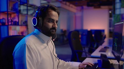 مفهوم صناعة الأفلام والإخراج، استخدام برامج تحرير متطورة لإنتاج الفيديوهات، إيماءات الاندماج و التركيز مع المؤثرات الصوتية والمرئية، تصويرمقرب من الجانب لمونتيرعربي خليجي سعودي يرتدي الثوب الابيض وسماعات الرأس يقوم  بالتأمل والإبداع الفني أمام الشاشة