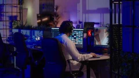 استخدام برامج تحرير متطورة لإنتاج الفيديوهات، التأمل والإبداع الفني أمام الشاشة، تصويرمن الخلف لمونتير عربي خليجي سعودي يرتدي الثوب الابيض و سماعات الرأس يقوم التفكير العميق والتحليل البصري