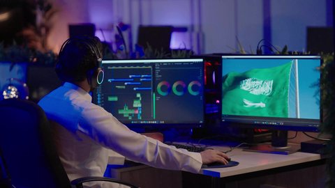 الإخراج السينمائي وصناعة المحتوى الإعلامي، التأمل والإبداع الفني أمام الشاشة، تصوير من الخلف لمونتيرعربي خليجي سعودي يرتدي الثوب الابيض و سماعات الرأس يقوم التفكير العميق والتحليل البصري