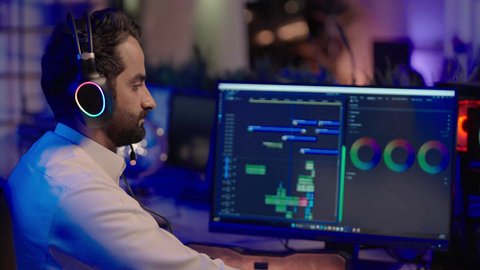 تحرير الفيديوهات باستخدام تقنيات رقمية متطورة، التأمل والإبداع الفني أمام الشاشة، تصوير مقرب من الجانب لمونتيرعربي خليجي سعودي يرتدي الثوب الابيض و سماعات الرأس يقوم التفكير العميق والتحليل البصري