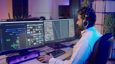 الاستفادة من برامج وتقنيات المونتاج الحديثة، تصوير من الجانب لمونتير عربي خليجي سعودي يرتدي الثوب الابيض  يضع سماعات الرأس ويقوم بتعديل الصوت على شاشة الكمبيوتر، صناعة الأفلام والبرامج التلفزيونية