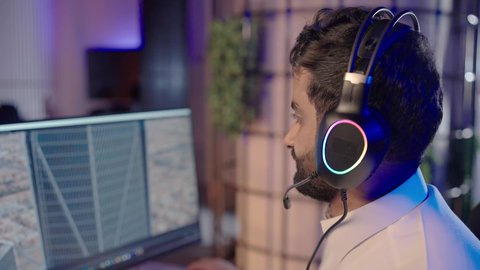 دمج المشاهد والمؤثرات المرئية، تصويرمقرب من الجانب لمونتير عربي خليجي سعودي يرتدي الثوب الابيض و سماعات الرأس يجلس أمام جهاز الحاسوب يستخدم برامج المونتاج لإضافة المؤثرات البصرية والصوتية، ايماءات الاندماج و التركيز