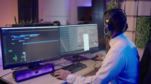 بيئة عمل احترافية في مجال الإعلام، تصوير من الجانب لمونتير عربي خليجي سعودي يرتدي الثوب الابيض و سماعات الرأس يجلس أمام جهاز الحاسوب يستخدم برامج المونتاج لإضافة المؤثرات البصرية والصوتية