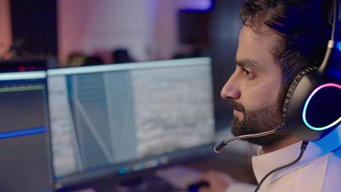 إدخال النصوص من خلال لوحة المفاتيح، استخدام التقنية الحديثة، الابتكار والإبداع في تصميم وإنتاج المحتوى المرئي، تصوير مقرب من الجانب لرجل عربي خليجي سعودي يرتدي الثوب الابيض يضع سماعة الراس يعمل في غرفة المونتاج يستخدم الحاسب المحمول لقص وترتيب المشاهد، ايماءات الاندماج و التركيز