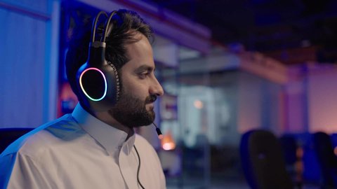 استخدام التقنيات الحديثة، تصوير من الجانب لمونتيرعربي خليجي سعودي يرتدي الثوب الابيض و سماعات رأس يعمل في استوديو، النظر الى شيء ما