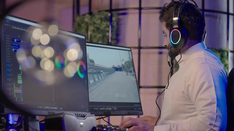 ايماءات الحيره و التردد، استخدام التقنية الحديثة، الابتكار والإبداع في تصميم وإنتاج المحتوى المرئي، تصويرمن الجانب لرجل عربي خليجي سعودي  يرتدي الثوب الابيض يضع سماعة الراس يعمل في غرفة المونتاج يستخدم الحاسب المحمول لقص وترتيب المشاهد يضع يده على ذقنه للتفكير فى شيء ما