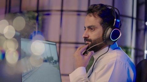 مفهوم الابتكار الفني في إنتاج المحتوى المرئي،  ايماءات الاندماج و التركيز، تصويرمن الجانب لرجل عربي خليجي سعودي  يرتدي الثوب الابيض يضع سماعة الراس يعمل في غرفة المونتاج يستخدم الحاسب المحمول لقص وترتيب المشاهد