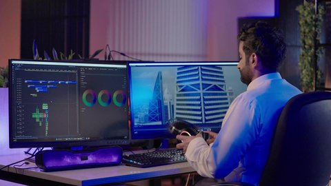 استخدام برامج المونتاج المتقدمة، تصويرمن الخلف لرجل عربي خليجي سعودي  يرتدي الثوب الابيض يضع سماعة الراس يعمل في غرفة المونتاج يستخدم الحاسب المحمول لقص وترتيب المشاهد، مفهوم صناعة المحتوى المرئي والإبداع الفني