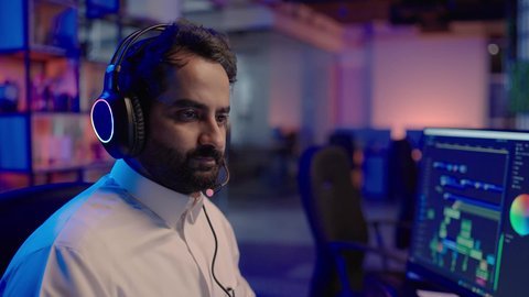 المونتاج وإنتاج الأفلام، تصوير لمونتير عربي خليجي سعودي يرتدي الثوب الابيض و سماعات الراس يجلس أمام شاشة حاسب محمول يقوم باخراج مشهد سينمائي ، ايماءات الاندماج و التركيز