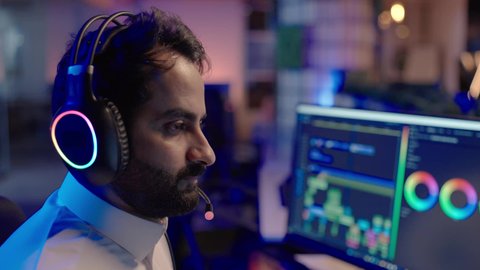 العمل على برامج المونتاج الاحترافية، تصوير من الجانب لمونتيرعربي خليجي سعودي يرتدي الثوب الابيض و سماعات الراس يجلس أمام شاشة حاسب محمول يقوم باخراج مشهد سينمائي  ، ايماءات الاندماج و التركيز