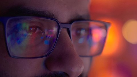 صناعة المحتوى الإعلامي، ايماءات الاندماج و التركيز، تصوير مقرب لوجه مونتيرعربي خليجي عماني يرتدي الدشداشة و الكمة والنظارة الطبية يركز على شاشة المونتاج