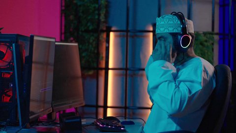 مفهوم الإبداع والإخراج الفني، تصوير من الجانب لمونتير عربي خليجي عماني يرتدي الدشداشة و الكمة وسماعات الرأس يجلس داخل الاستديو يتابع شاشة المونتاج لمراجعة مقاطع الفيديو وإنتاج الأفلام، دمج المشاهد والمؤثرات المرئية