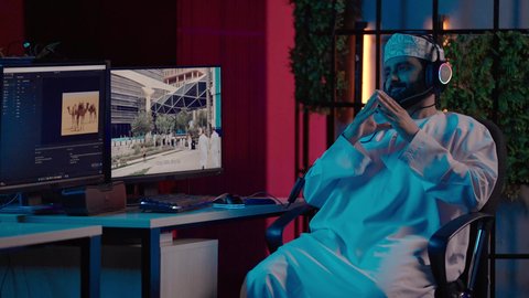 تعابير السعادة و السرور، تصوير لمونتير عربي خليجي عماني يرتدي الدشداشة و الكمة وسماعات الرأس يجلس داخل الاستديو ينسجم مع المؤثرات الصوتية والمرئية،الإبداع في مجال الميديا