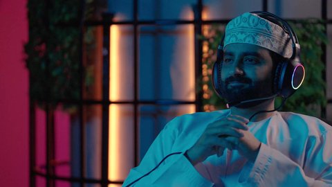 إيماءات الانسجام مع المؤثرات الصوتية والمرئية، استخدام برامج تحرير متطورة لإنتاج الفيديوهات، تصوير لمونتيرعربي خليجي عماني يرتدي  الدشداشة و الكمة وسماعات الرأس يقوم بالتأمل والإبداع الفني أمام الشاشة