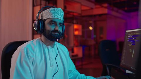 المونتاج والإبداع الفني، لمونتير عربي خليجي عماني يرتدي الدشداشة و الكمة و سماعات الرأس يركز على شاشة الكمبيوتر لإخراج مشهد متكامل، التحكم في الانتقالات والمؤثرات