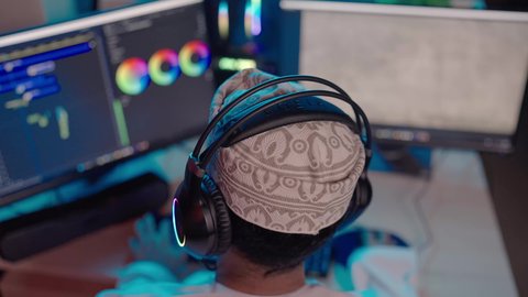 استخدام برامج تحرير متطورة لإنتاج الفيديوهات، تصوير مقرب من الخلف  لمونتير عربي خليجي عماني يرتدي الدشداشة و الكمة و سماعات الرأس يقوم بمشاهدة شاشة المونتاج، مفهوم صناعة الأفلام والإخراج