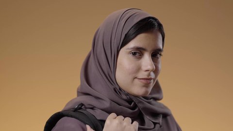 الاستعداد للعام الدراسي الجامعي الجديد, النظر إلى الكاميرا بإيماءات الثقة بالنفس، بورتريه مقرب لطالبة جامعية عربية سعودية خليجية تحمل الحقيبة الجامعية, تلميذة مجتهدة متشوقة للذهاب الى الجامعه, التعليم في مدارس وجامعات المملكة العربية السعودية , خلفية زرقاء.