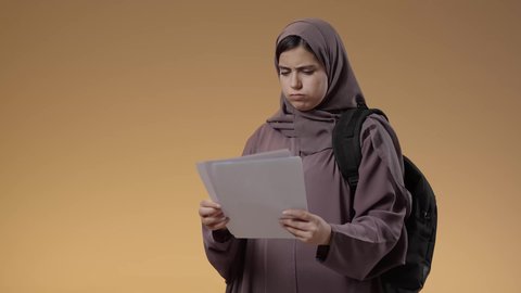 ايماءات وتعابير الاستياء والغضب، التشوق للذهاب إلى الجامعه, الاستعداد للعام الدراسي الجامعي الجديد, بورتريه لطالبة جامعية عربية سعودية خليجية تحمل الحقيبة الجامعية وتمسك بيديها اوراق بيضاء, التعليم في مدارس وجامعات المملكة, المذاكرة والاجتهاد والدراسة، خلفية بني.