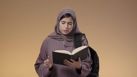 Eagerness to go to university, spending time learning and educating oneself, preparing for the new academic year, portrait of a Saudi Arabian Gulf female university student carrying her university bag and reading a book, education in the schools and universities of the Kingdom, studying, hard work and studying, blue background.