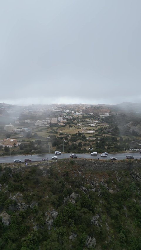 The rocky mountain ranges of Abha and Namas, the rough terrain and stone roads, aerial photography of the mountainous environment in the Asir region, the white clouds and foggy atmosphere covering the high peaks, the green nature and beautiful parks and gardens, the trees and plants on the mountain slopes