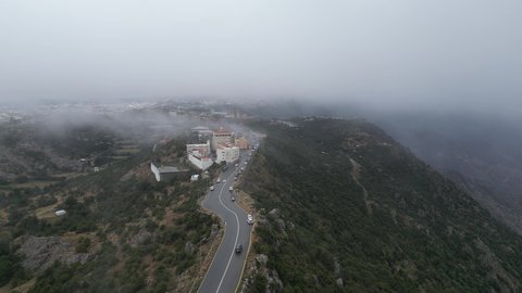 سلاسل جبال أبها والنماص الصخرية، التضاريس والطرق الحجرية الوعرة، تصوير جوي للبيئة الجبلية في منطقة عسير، السحب البيضاء والجو الضبابي المغطي للقمم العالية، الطبيعة الخضراء والمنتزهات والحدائق الجميلة، الأشجار والنباتات على سفوح الجبل