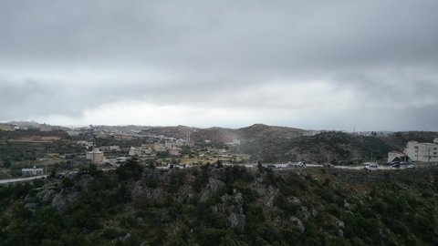 سلاسل جبال أبها والنماص الصخرية، التضاريس والطرق الحجرية الوعرة، تصوير جوي للبيئة الجبلية في منطقة عسير، السحب البيضاء والجو الضبابي المغطي للقمم العالية، الطبيعة الخضراء والمنتزهات والحدائق الجميلة، الأشجار والنباتات على سفوح الجبل