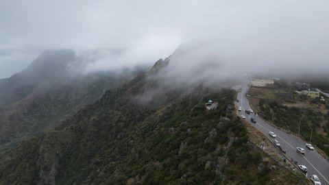 سلاسل جبال أبها والنماص الصخرية، التضاريس والطرق الحجرية الوعرة، تصوير جوي للبيئة الجبلية في منطقة عسير، السحب البيضاء والجو الضبابي المغطي للقمم العالية، الطبيعة الخضراء والمنتزهات والحدائق الجميلة، الأشجار والنباتات على سفوح الجبل